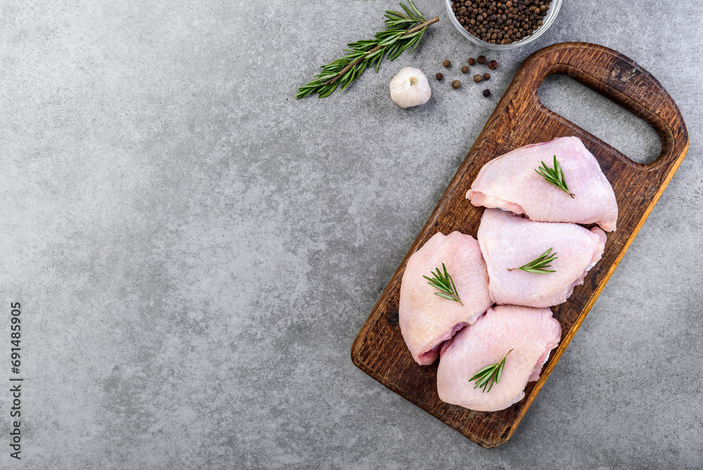 Raw chicken thighs on wooden board on gray background.