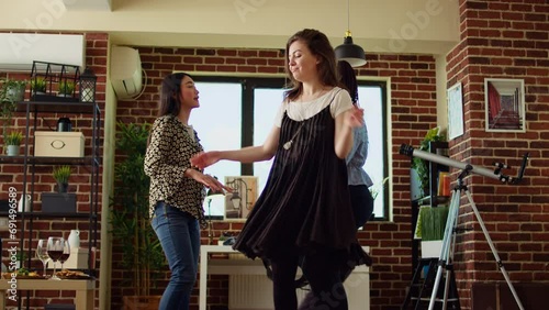 Happy friends dancing at apartment party, having fun together, rotating and jumping around. Mates doing energetic dance moves on upbeat songs in stylish living room, hip level shot