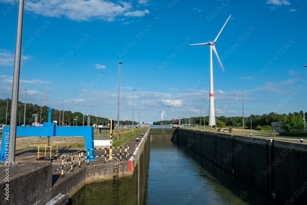 This vibrant image features a maritime lock system on a clear day, set against a backdrop of sustainable energy with a towering wind turbine. The locks serve as critical infrastructure for managing This vibrant image features a maritime lock system on a clear day, set against a backdrop of sustainable energy with a towering wind turbine. The locks serve as critical infrastructure for managing