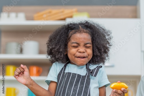 african afro hair black kid Cute taste oranges citrus sour flavour on ripe mouth in kitchen. candid back african daughter kid afro hair frowning face in taste feelings mood sour with sliced oranges. photo