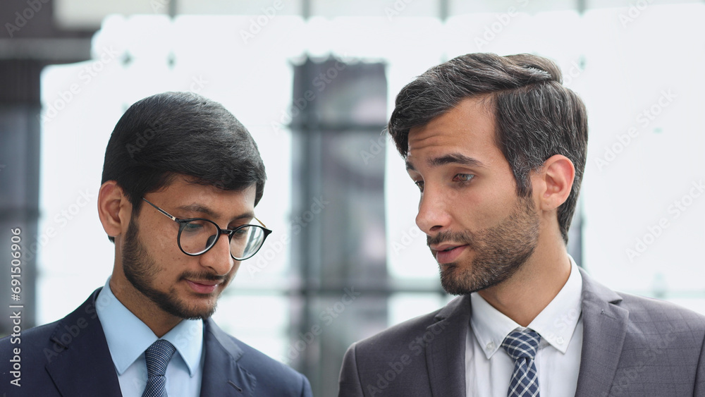 Business executive man and colleague standing in modern office hallway discussing project. Business executive man and colleague standing in modern office hallway discussing project.