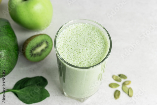 Green detox smoothie, blended vegetarian drink, protein milkshake in a glass from spinach, apple, avocado, kiwi and seeds on a table, healthy eating concept