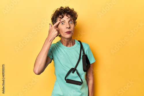 Sportswoman with resistance bands on yellow showing a disappointment gesture with forefinger.