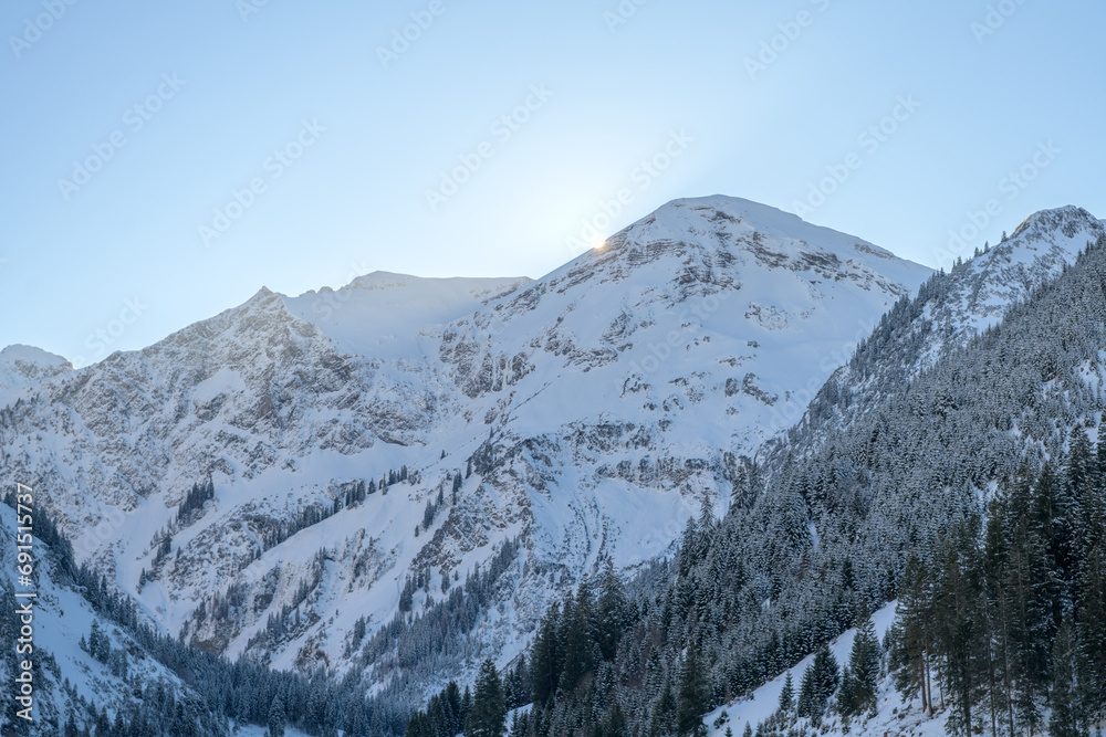 The sun sets behind the mountains at Vilsalpsee. Snow-covered cold winter day The sun sets behind the mountains at Vilsalpsee. Snow-covered cold winter day