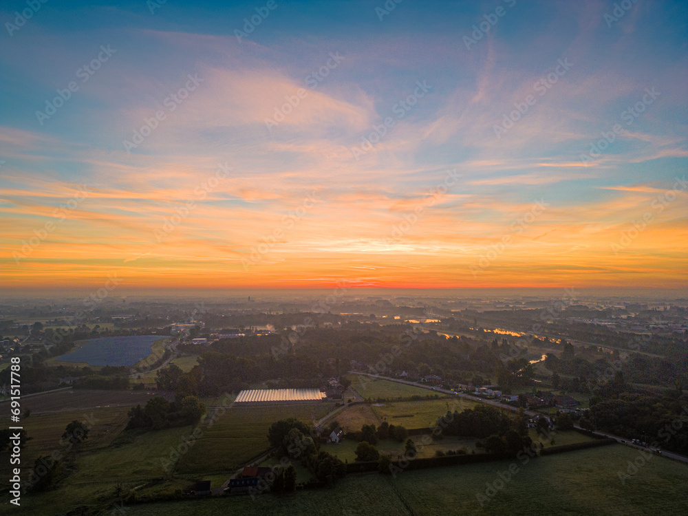 Captured at the break of dawn, this image showcases the serene beauty of the countryside bathed in the soft, warm glow of sunrise. The sky, painted in strokes of orange, pink, and blue, reflects over