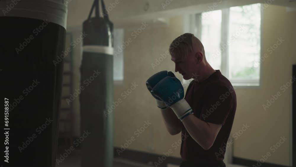 Boxer fights punching bag in empty gym. Strong man in boxing gloves punches hanging bag in fighting club slow motion. Martial arts master Boxer fights punching bag in empty gym. Strong man in boxing gloves punches hanging bag in fighting club slow motion. Martial arts master