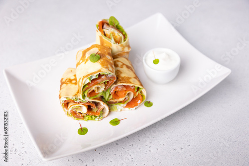 Pancakes with salmon (trout), sour cream and greenstuff. Thin, not sweet blinchiki stuffed with red fish. Traditional Russian and Ukrainian dish. Feast of Maslenitsa. Selective focus, close-up. photo