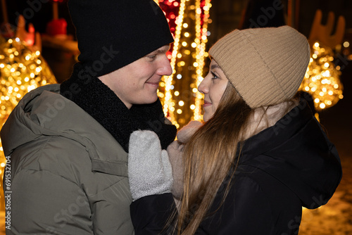 Positive, cheerful couple hugging during x-mas evening. Decorated lights on the streets outdoors (ID: 691532704)