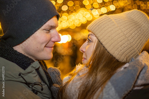 Positive, cheerful couple hugging during x-mas evening. Decorated lights on the streets outdoors (ID: 691532713)