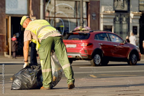A male janitor removes garbage bags from the streets of the city. The city service takes care of the cleanliness and order in town.