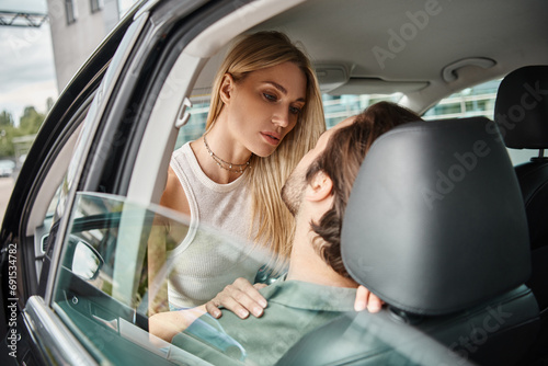 attractive blonde woman seducing man sitting in modern car on urban street, romantic love dating photo