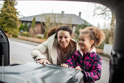 Happy mother and daughter put their suitcase in car trunk