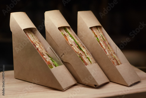 Sandwiches in paper takeaway triangle zero waste boxes on dark background. Snack food, eating at office. Close up.