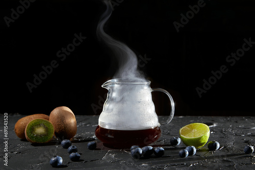 Hot coffee in a glass teapot on a black stone table with fruit. © Лев Малевич