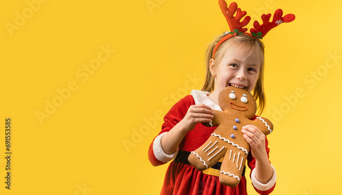 Cute little girl wearing Santa red costume and holding big baked gingerbread man cookie on the yellow background. Portrait of a happy smiling 5 year old girl on the Christmas background photo