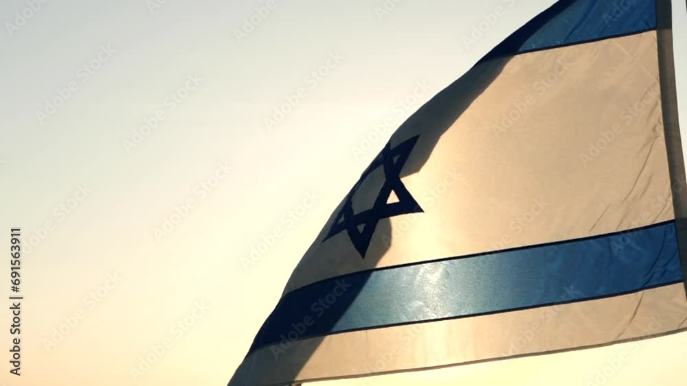 Israel flag with star of David over the sunset, waving against the wind, cloudy sky background. Concept of Israel, National flag, Memorial Day, Independence Day, Holiday, Palestine, Conflict, Freedom