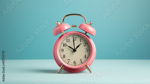 Pink vintage alarm clock with black hands and numerals, standing on a surface with a blue background.