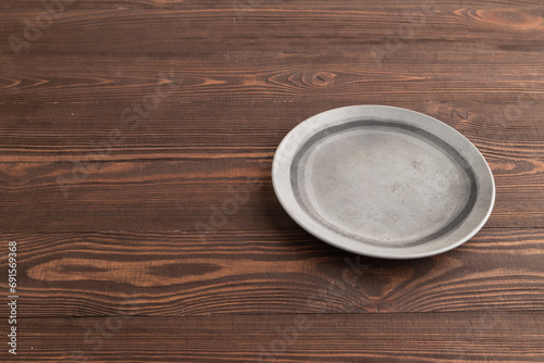 Empty gray ceramic plate on brown wooden. Side view, copy space