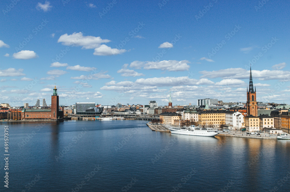 panoramic view of rooftops and view of the town hall tower with many colorful houses in stockholm and water channels huge boat and cloudy sky