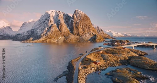 Aerial view of snowy rocks, islands with rorbuer, sea bay, bridge, mountains, road, purple sky at sunrise in winter. Amazing top drone view of rorbu in Hamnoy village, Lofoten islands, Norway. Travel