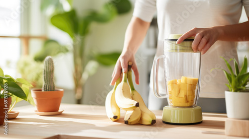 Person's hand preparing to make a smoothie, with bananas in one hand and chopped mango pieces in a blender photo