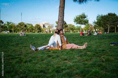 Happy gay couple sitting on grass in park on sunny day