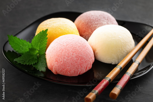 Dessert tender delicious mochi on a black plate with mint leaves and bamboo chopsticks. Close-up. View from above. Perfect retouching. Advertising.