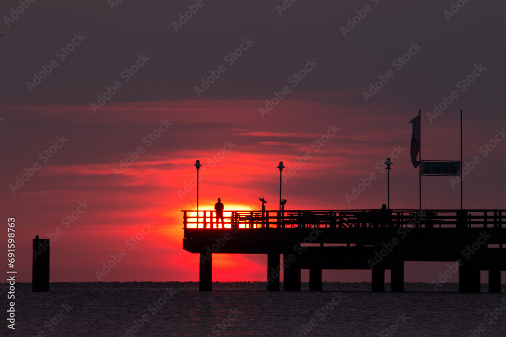 Fischer im Sonnenuntergang auf einer Seebrücke  - obrazy, fototapety, plakaty 