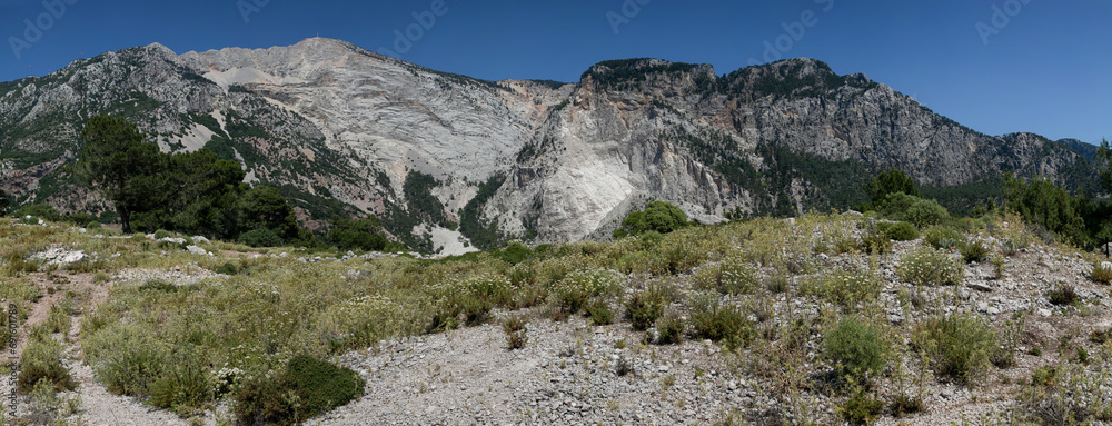 Wide green meadow against the background of high misty mountain ranges. Mediterranean mountain landscape: steep slopes, high rocky cliffs, greenery. Wide green meadow against the background of high misty mountain ranges. Mediterranean mountain landscape: steep slopes, high rocky cliffs, greenery.