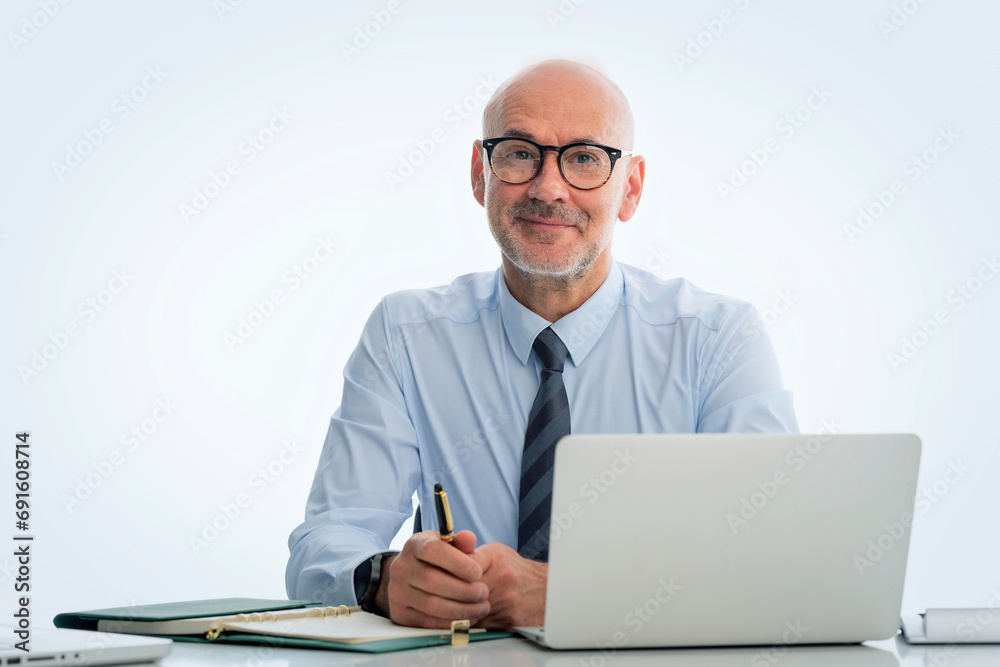 MId aged businessman sitting at desk and using laptop against at isolated white background MId aged businessman sitting at desk and using laptop against at isolated white background