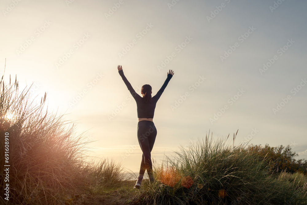 sporty woman with arms up celebrating goals after sport exercising and working out outdoors after a morning run