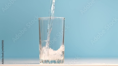 Crystal-clear water pours into a glass, capturing a moment of purity and refreshment against a soothing blue backdrop.