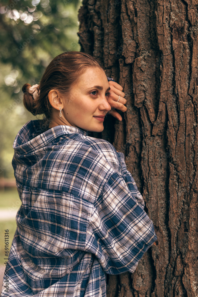 Portrait of a young attractive woman leaning her face against a tree trunk on a summer day.Self-care,healthy lifestyle,mental health,eco-friendly concept. Portrait of a young attractive woman leaning her face against a tree trunk on a summer day.Self-care,healthy lifestyle,mental health,eco-friendly concept.