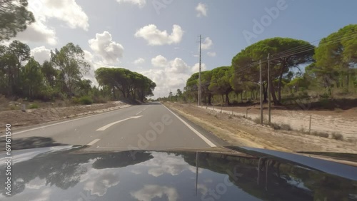 First person view, FPV, from dashcam of car driving along the Alentejo Coast in Portugal, passing cork oak trees and sand dunes. Road trip video in POV, with blue sky and clouds on an empty road photo