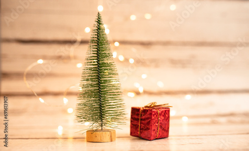 small Christmas tree with a gift on a light wooden background