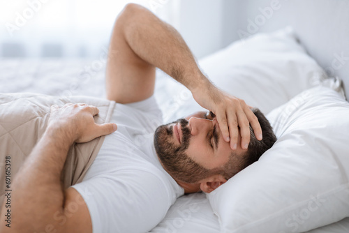 Man awake in bed suffering from headache touching forehead indoors photo