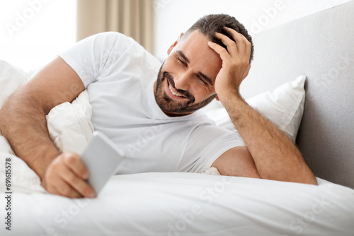 man lying in bed and using cellphone sending messages indoor