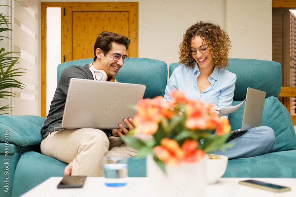 Happy couple sitting on couch while working on laptop at home Happy couple sitting on couch while working on laptop at home