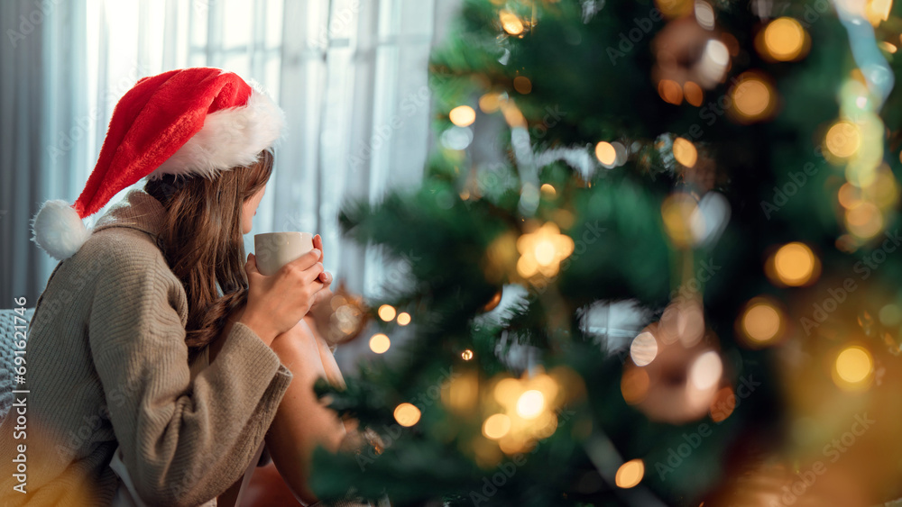 Alone beautiful charming asian woman drinking coffee on xmas Eve at living room with festive interior, Side view of young female with cup sitting by window at home at Christmas time