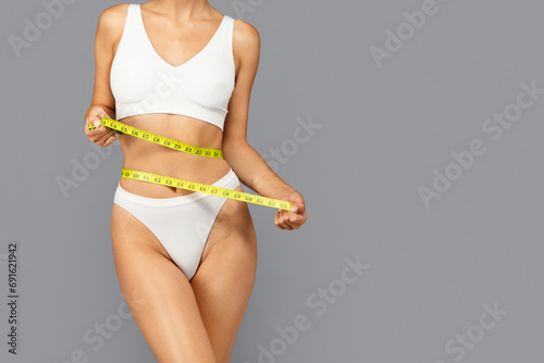 European woman in white sports bra and panties holds yellow measuring tape around waist photo