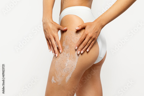 Close up of european young lady applying exfoliating scrub on thigh, showcasing a self-care