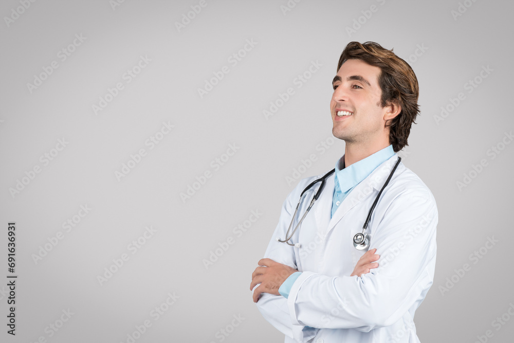 Confident male doctor looking aside posing near empty space for medical advertisement text or design, grey background Confident male doctor looking aside posing near empty space for medical advertisement text or design, grey background