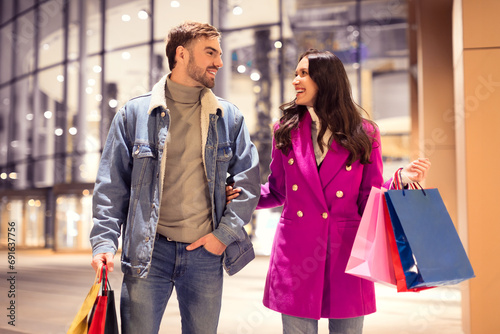 Millennial couple enjoying winter shopping trip carries bags outside mall photo