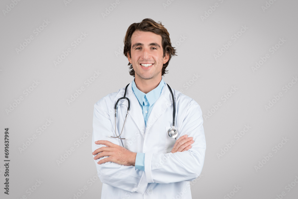 Portrait of cheerful man doctor posing with crossed arms and smiling at camera isolated over grey studio background Portrait of cheerful man doctor posing with crossed arms and smiling at camera isolated over grey studio background