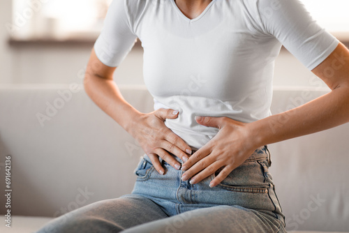 Unrecognizable young woman touching aching stomach feeling abdominal pain indoor photo