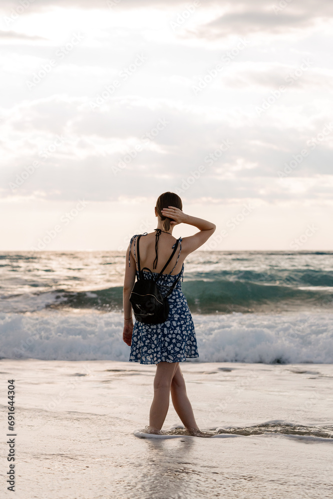 A solitary woman stands on the beach, looking out to the waves at sunset A solitary woman stands on the beach, looking out to the waves at sunset