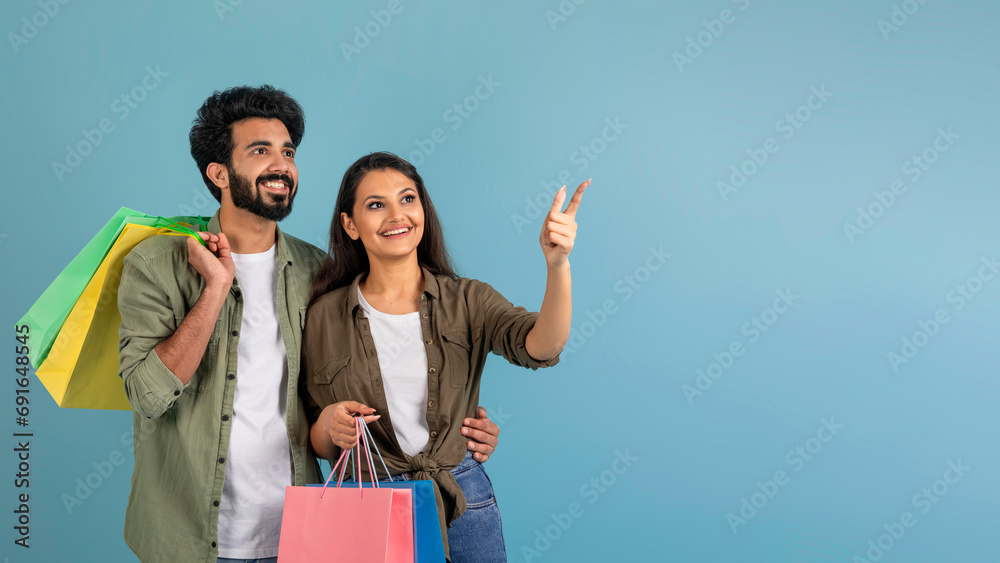 Happy young eastern couple shopaholics pointing at copy space Happy young eastern couple shopaholics pointing at copy space