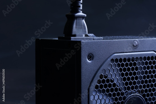 Modern computer AC power supply unit with a powerful fan and a connected power cable on a dark background. Fragment. A device for power supply of a modern personal computer. Photo photo