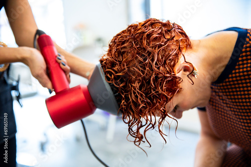 Professional hairstylist drying curly hair with blow dryer photo