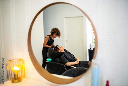 Hairstylist washing client's hair in a salon mirror reflection photo